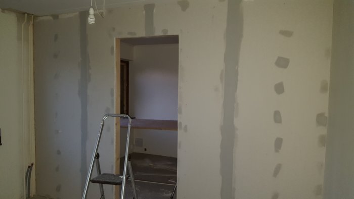 Renoveringsarbete på ett stort rum med spacklade väggar och en stege.