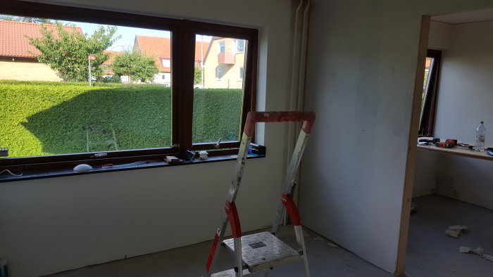 Renoveringsprojekt av ett stort rum med stege framför fönstret och byggmaterial på golvet.