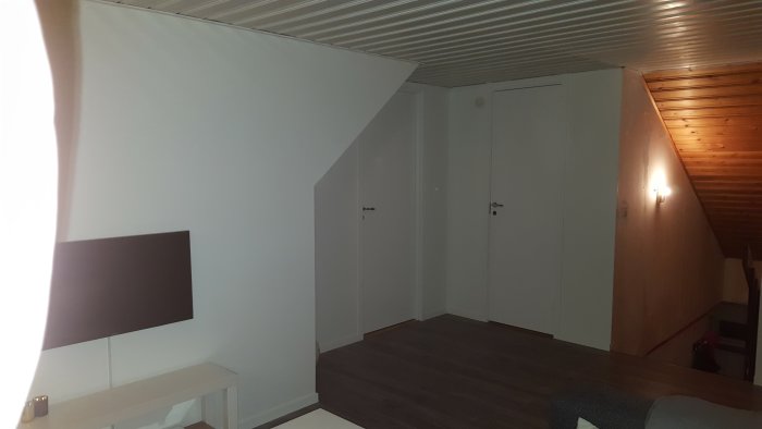 Del av ovanvåning med vitmålade garderobsväggar, träpaneltak och mörkt laminatgolv.