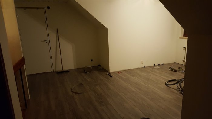 Delvis renoverad ovanvåning med nytt golv, vita väggar och renoveringsmaterial på golvet.