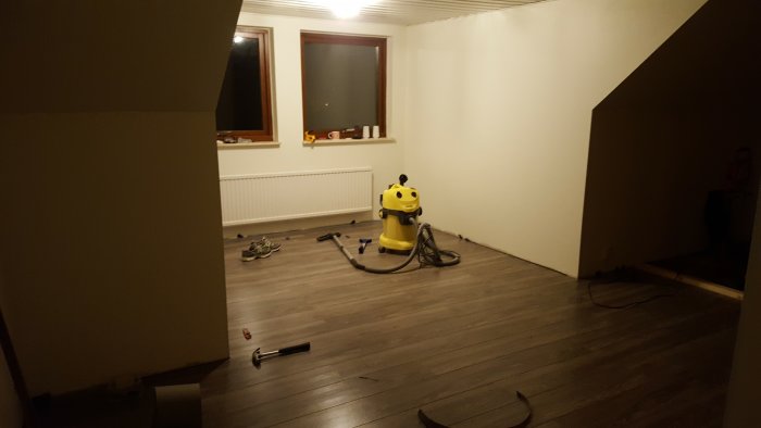 Ovanvåning under renovering med trägolv, dammsugare och verktyg på golvet.