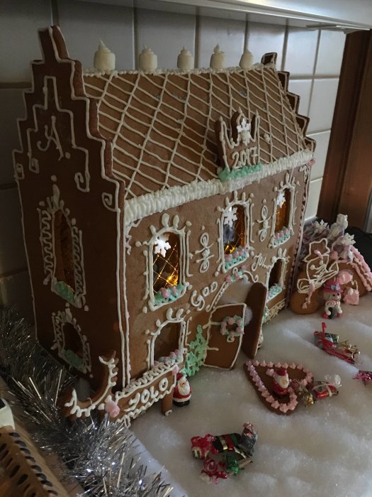 Handgjort pepparkakshus med dekorativa detaljer och belysning på en juldekorerad skiva.