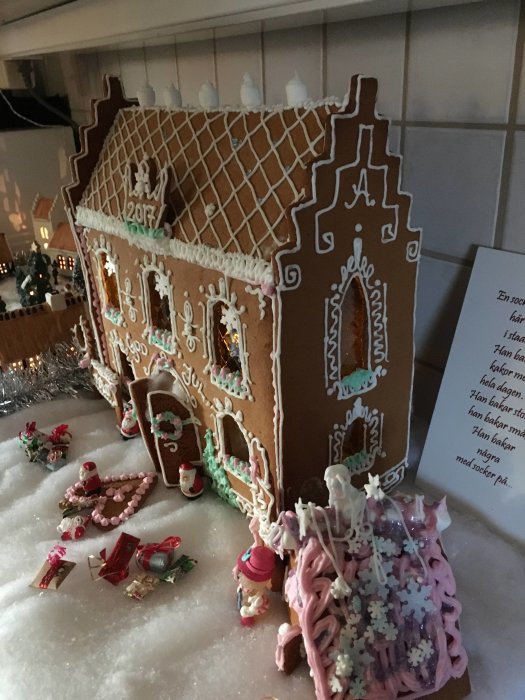 Stort handbyggt pepparkakshus med dekorationer, belysning och snöliknande underlag.