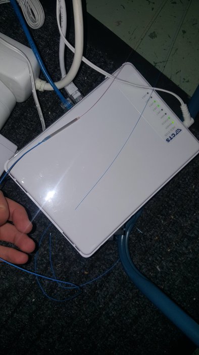 Router med lösa blå och vita kablar och metalldetaljer synliga på grått underlag.