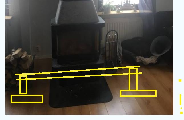 Kamin på en svart plåt med skissade lyftanordningar i gult runtom, inomhusmiljö.