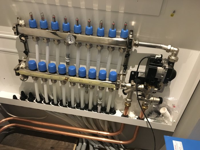 Golvvärmeinstallation med fördelare, termostatventiler och cirkulationspump i skåp.