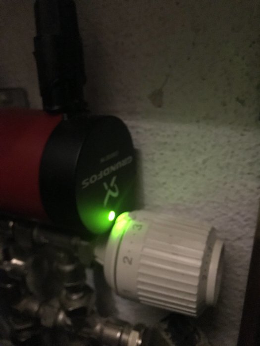 Värmesystem med grön lysande pump och en manuell vred för fjärrvärmeinställningar.