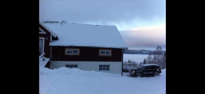 Exteriör av vitkalkad lada med snötäckt tak mot vinterlandskap i Jämtland.