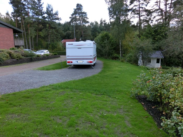 Trädgård med nyanlagt grusområde för parkering av en vit husvagn, omgiven av grönt gräs och buskplanteringar.