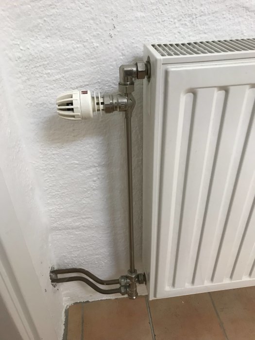 Thermostatventil och kopparanslutning på radiator med övergång från järnrör.