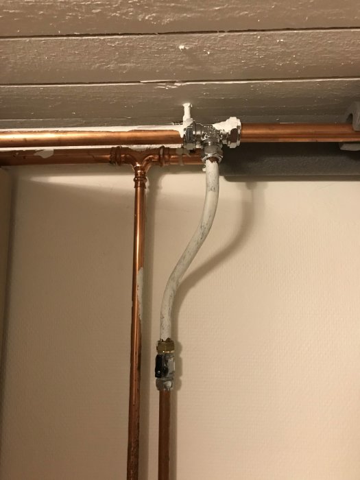 Kopparledningar kopplade till en ventil och en övergång från järnrör vid ett tak.