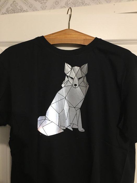 Svart T-shirt med geometrisk rävdesign i vinyl hängande på en klädhängare.