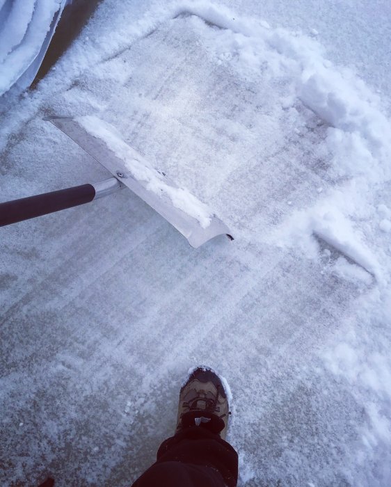 Person som skottar snö nära huset med en synlig snöskyffel och snöig mark.