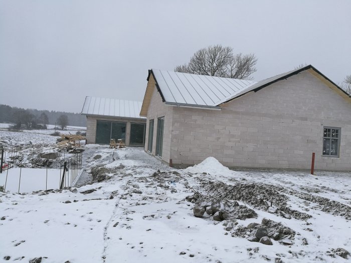 Ett nybyggd hus med tegelväggar och snö på taket i vinterlandskap, byggarbetsplats i förgrunden.