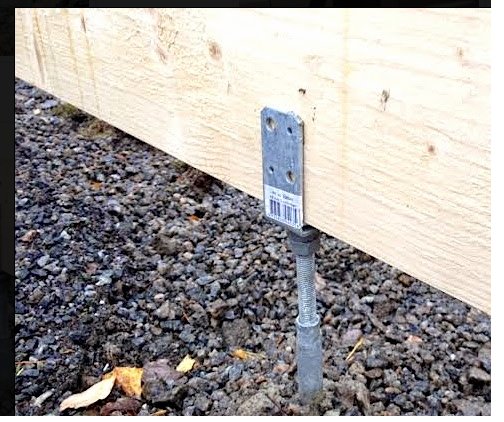 Justerbar stolpsko monterad på mackadam under träregel för byggprojekt.