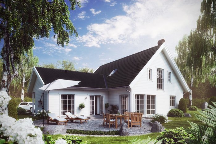 Vinkelbyggnad med vit fasad och svart tak, omgiven av en välskött trädgård och uteplats med möbler.