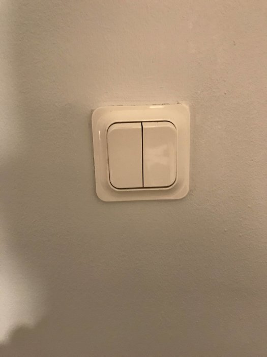 Väggmonterad ljusströmbrytare i vitt mot en grå vägg.