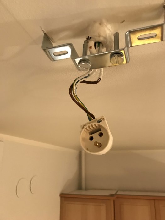 Takmonterad eluttagsdosa med öppna kablar och metallfäste framför vit vägg ovanför köksskåp.