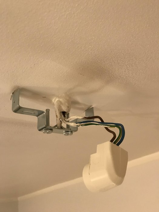 Omonterad taklampa med synliga anslutningskablar och fästjärn mot en vit takyta.