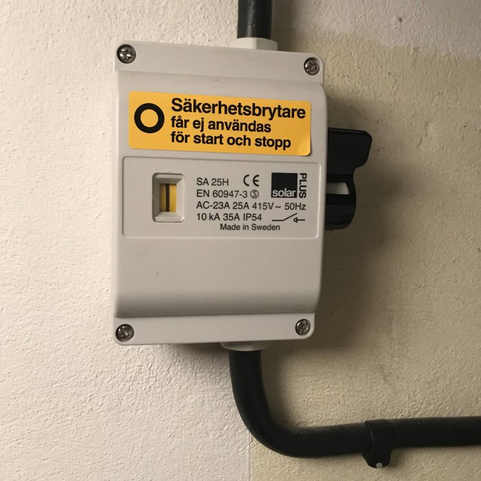 Säkerhetsbrytare på vägg med varningstext "får ej användas för start och stopp", inkopplad med svart kabel.