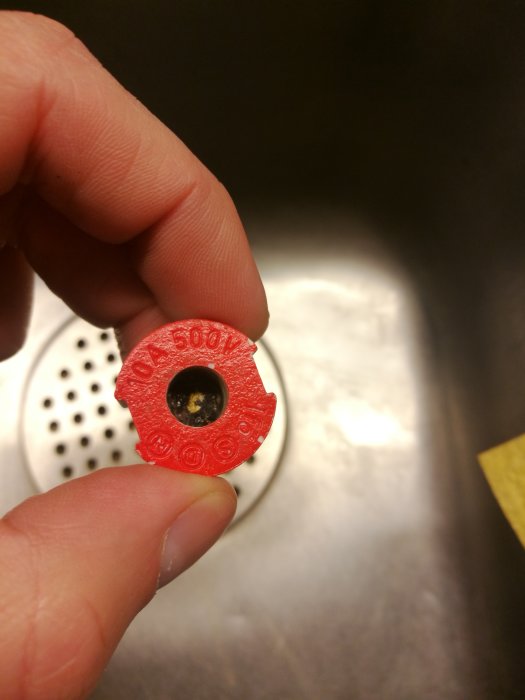 Närbild av en hand som håller en röd, sliten bottenplatta ovanför en vit yta.