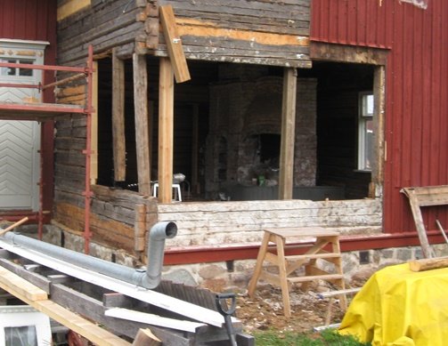 Renovering av en gammal timmerstuga med en stor öppning i fasaden och stödstrukturer runtom.