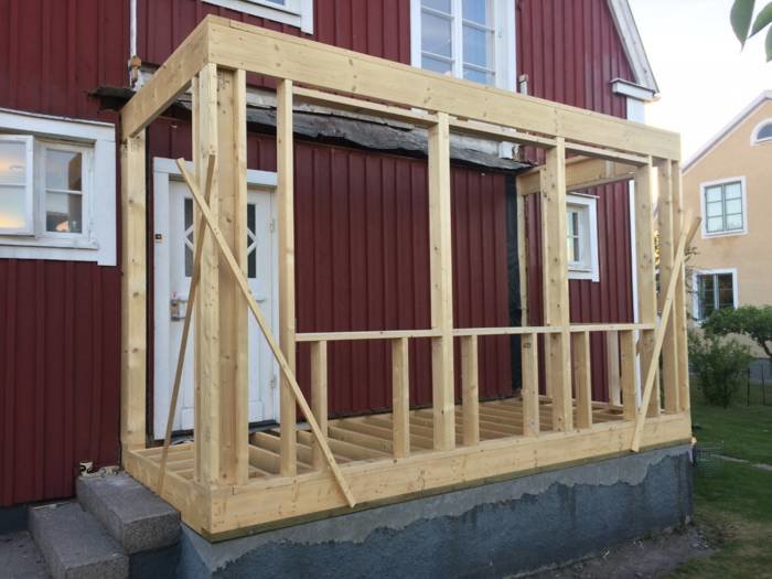 Träregelverk för ett byggprojekt med en övre stående regel framför en röd husvägg.