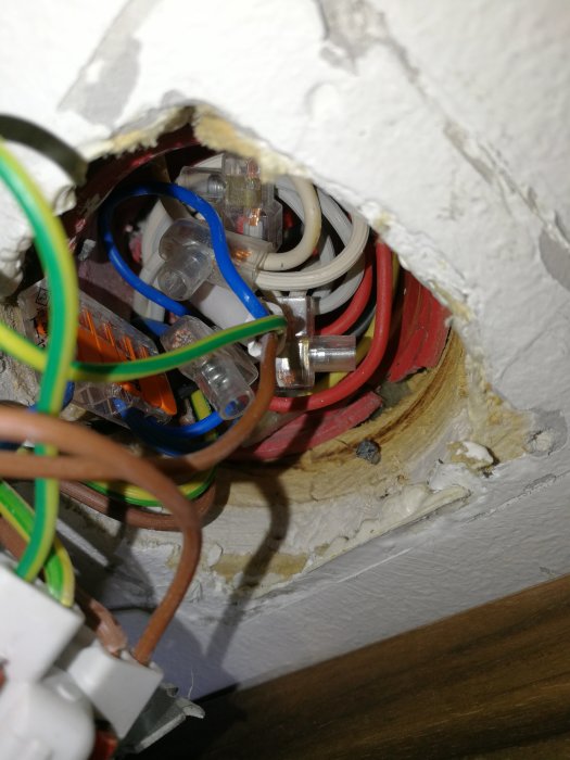 Elinstallation med trånga kablar genom hål i en väggdosa, lös isolering syns, tecken på slarvigt elarbete.