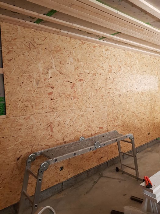 Isolerat garage med nyinstallerade OSB-skivor på väggen och en uppfälld arbetsbock i förgrunden.