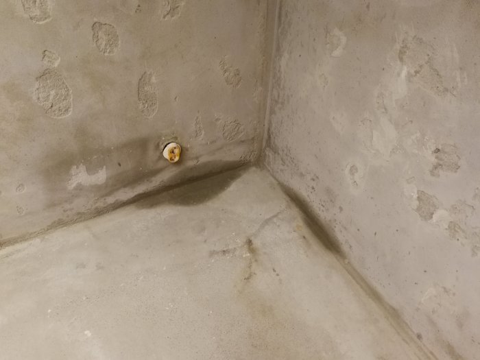 Fuktfläck i hörnet av ett avskalat betonggolv och vägg i källarförråd, mönster av fukt syns på ytan.