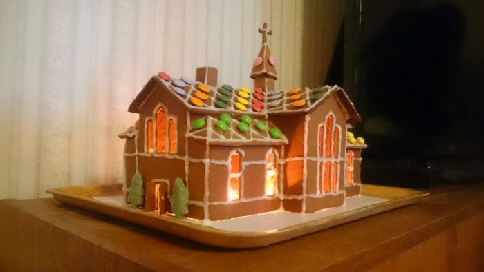 Pepparkakshus modellerat som en kyrka med dekorativa godis och tänt ljus inuti.