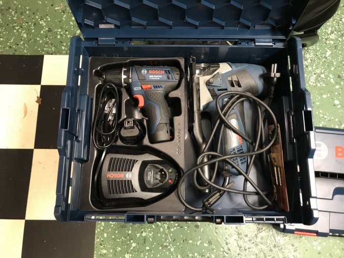 En öppen blå verktygslåda med en borrmaskin och en slipmaskin organiserade inuti, på ett klinkergolv.