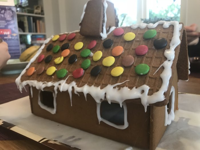 Hemgjord pepparkakshus dekorerad med färgglada godis och vit glasyr på taket.