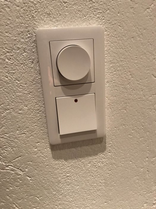 En Exxact strömställare och dimmer monterad på en texturerad vägg.