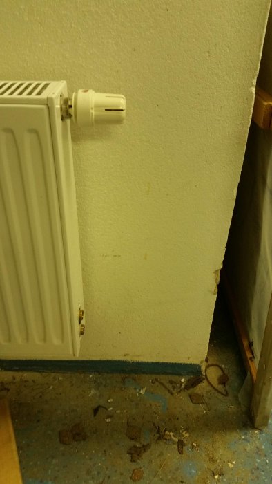Radiator nära vit vägg med synliga röraanslutningar och avstånd markerat för installation.