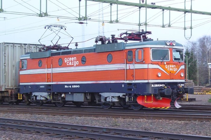 Green Cargo RC4-lok nummer 1290 på järnvägsspår med en fraktcontainer i bakgrunden.