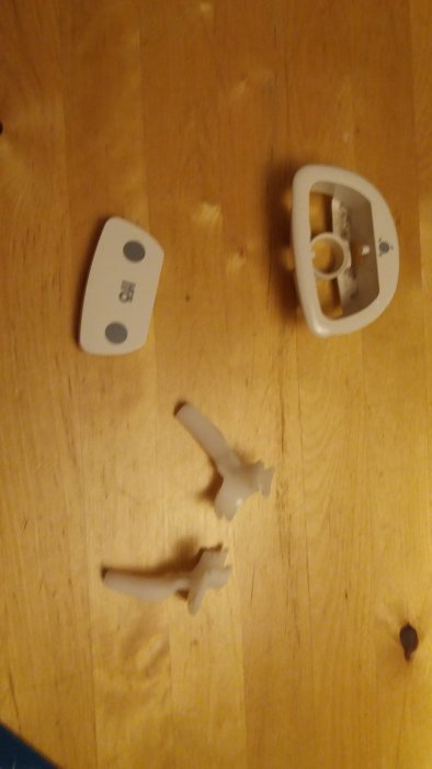 Sönderdelad toalettspolknapp i tre delar på ett trägolv.
