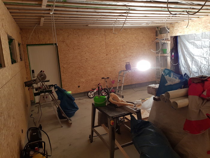 OSLätt renoveringsarbete i ett garage med OSB-väggar, verktyg och byggmaterial.