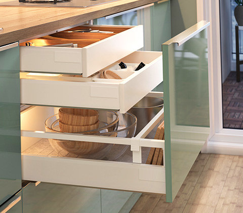 Öppna vita kökslådor med inredningslösningar, en med dold innerlåda och köksartiklar inuti.