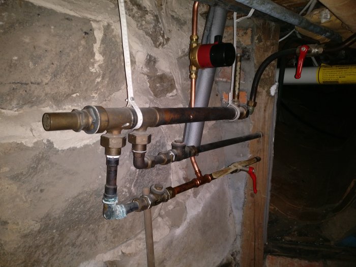 Rörinstallation med olika typer av rör och ventiler på en stenmur i ett renoveringsprojekt.