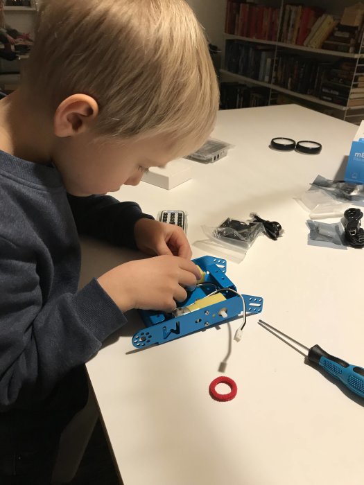 Barn bygger en robot med delar och skruvmejsel på ett vitt bord.