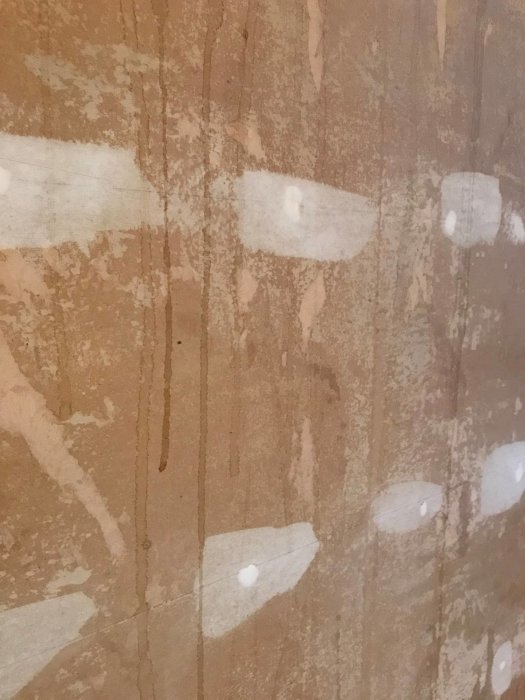 Närbild av en vägg där tapeten rivits bort, exponerande gips och masonitliknande material.