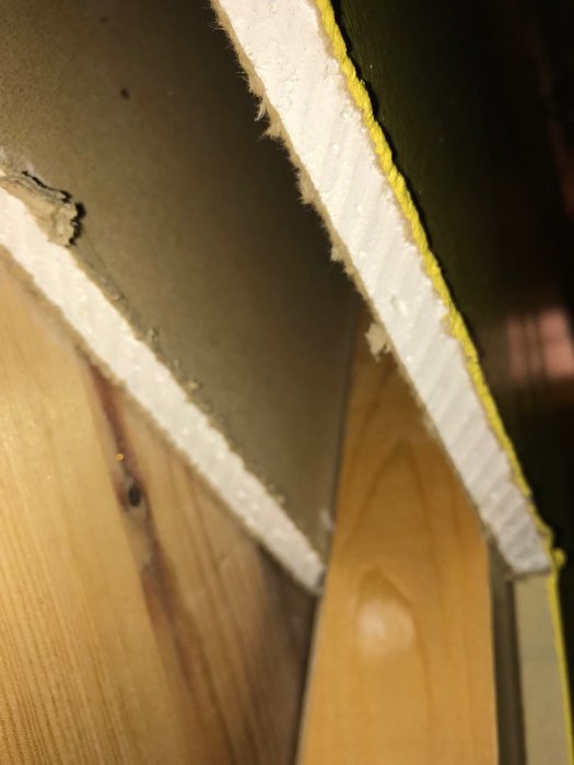 En bild som visar ett hörn av ett rum med avriven tapet som avslöjar gips och masonitmaterial under.