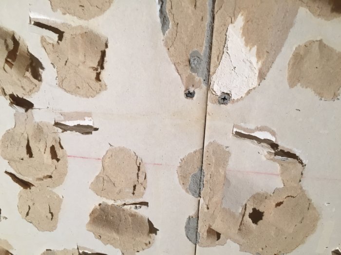 Vägg med borttaget gammalt kakel visar rester av lim, tapet och delvis exponerat gips.