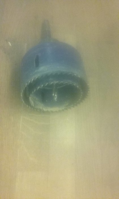 En stor 63mm hålsåg monterad i en hållare, med en mindre 58mm hålsåg gängad inuti som styrning, på en suddig bakgrund.