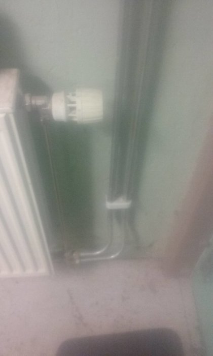 Suddig bild av ett pannrum med radiator och termostat samt väl böjda rörledningar mot golvet.