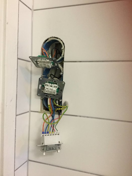 Öppen elinstallation med brytare och synliga kablar på ett kaklat badrumsvägg, fokus på grå kabel.