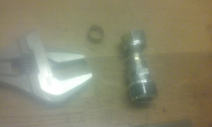 Rördelar och en skiftnyckel på en träyta, innehåller en metalldel och en klämring. Bilden är suddig.