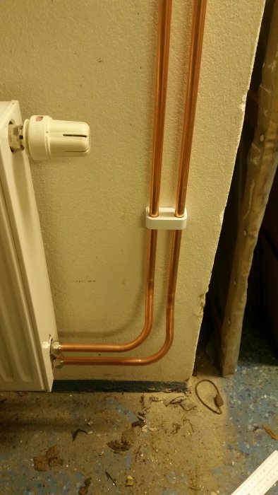 Kopparrör böjda och installerade vid vägg intill en radiator, några isolerade rör syns i bakgrunden.