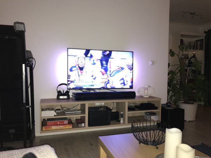 TV på bänk med sportprogram på skärmen, soundbar och diverse föremål runtomkring i ett vardagsrum.